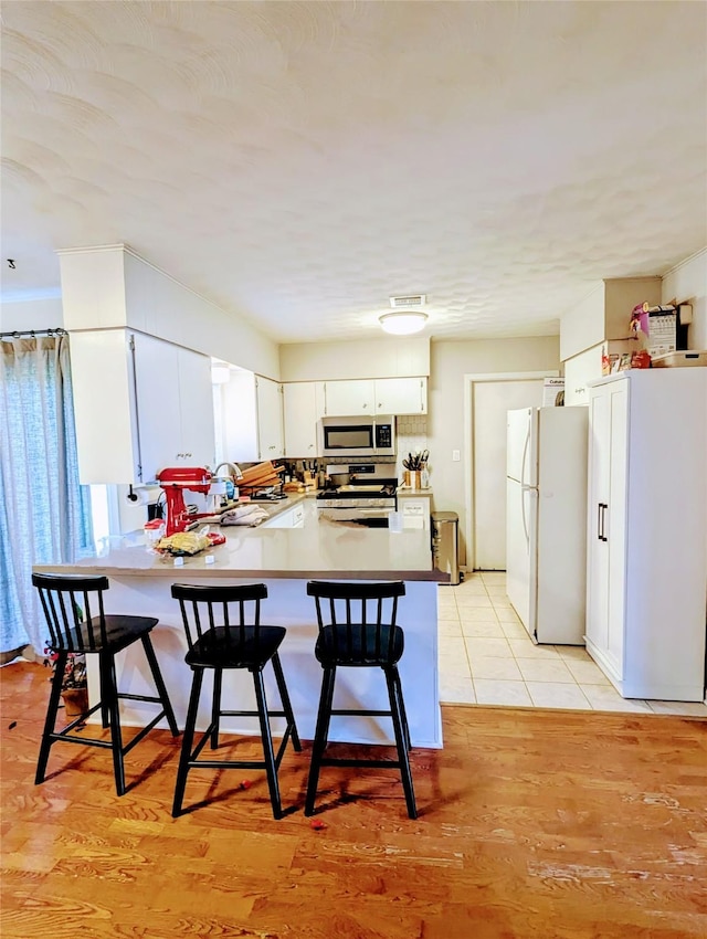 kitchen featuring a kitchen bar, a peninsula, white cabinets, and stainless steel appliances