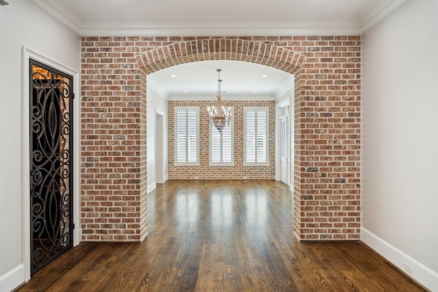 unfurnished dining area with crown molding, a notable chandelier, dark wood-style floors, and brick wall