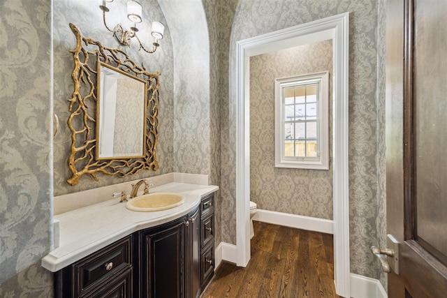 bathroom featuring toilet, wood finished floors, wallpapered walls, baseboards, and vanity