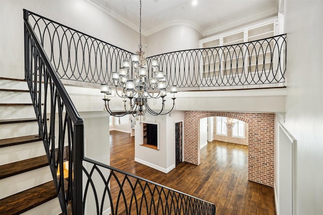 stairway with wood finished floors, an inviting chandelier, a towering ceiling, and crown molding