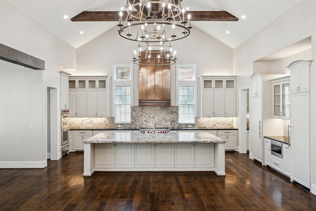 kitchen with decorative backsplash, beamed ceiling, a kitchen island with sink, and dark wood-style flooring