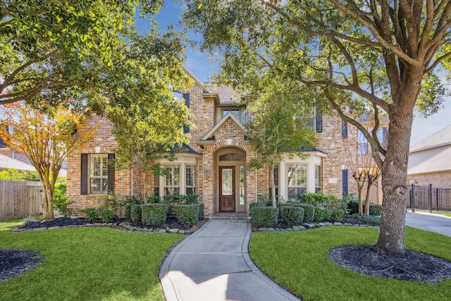 view of front of house featuring brick siding, a front lawn, and fence