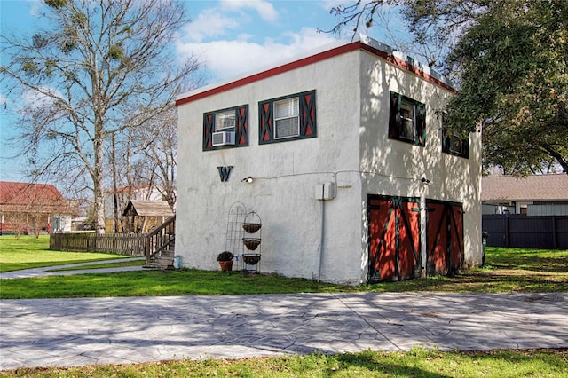 view of side of property with a yard, fence, driveway, and stucco siding