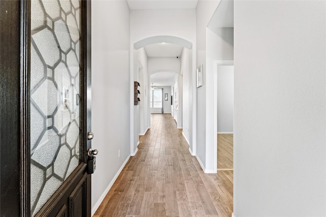 corridor featuring arched walkways, light wood finished floors, and baseboards