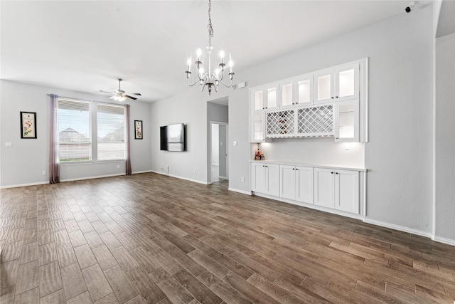 unfurnished living room featuring ceiling fan with notable chandelier, dark wood-type flooring, and baseboards