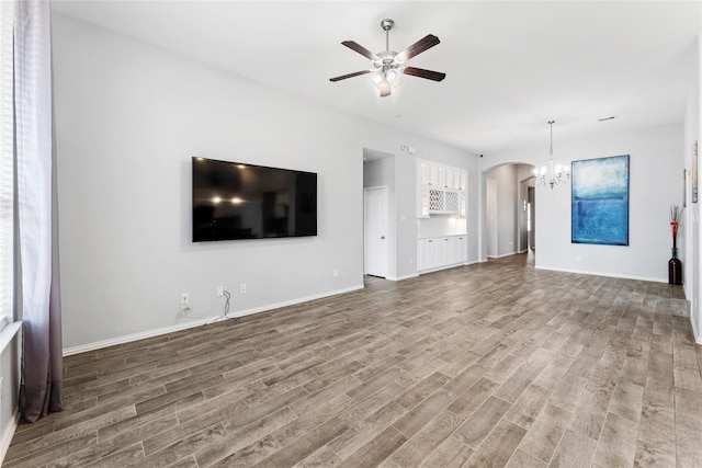 unfurnished living room featuring wood finished floors, ceiling fan with notable chandelier, arched walkways, and baseboards