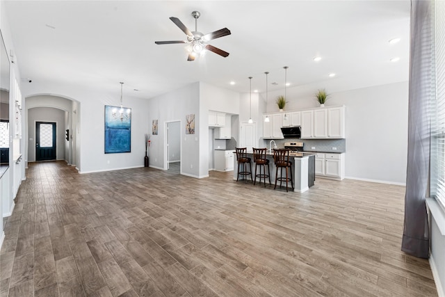 unfurnished living room featuring ceiling fan with notable chandelier, arched walkways, light wood finished floors, and baseboards