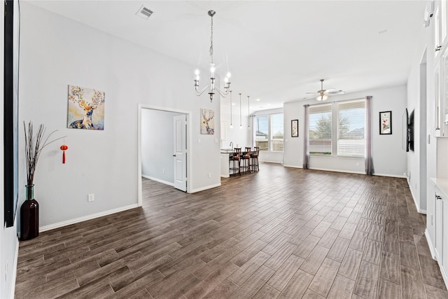 unfurnished living room with dark wood-type flooring, ceiling fan with notable chandelier, visible vents, and baseboards