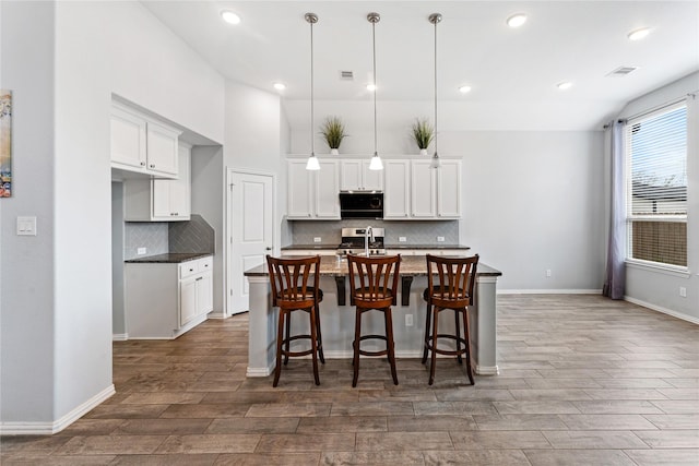 kitchen with stainless steel gas stove, visible vents, a center island with sink, and wood finish floors