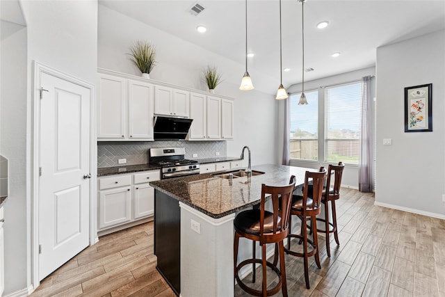 kitchen featuring visible vents, wood tiled floor, gas range, decorative backsplash, and a sink