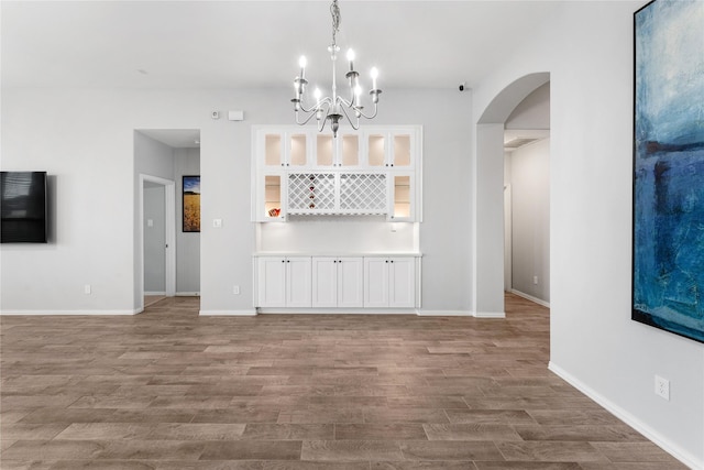 unfurnished living room featuring baseboards, wood finished floors, arched walkways, and a chandelier