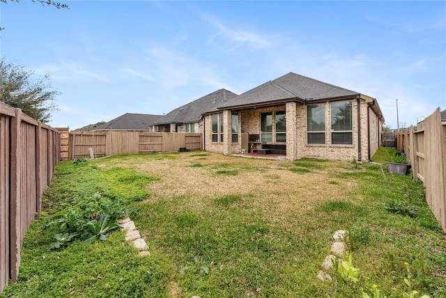 rear view of property with a yard, brick siding, roof with shingles, and a fenced backyard