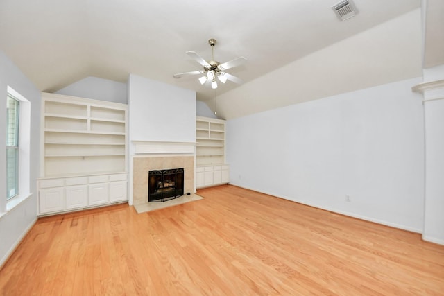 unfurnished living room featuring wood finished floors, a ceiling fan, visible vents, vaulted ceiling, and a tiled fireplace