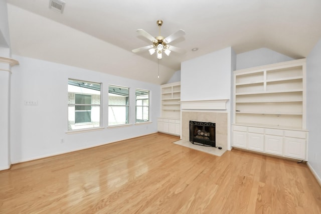 unfurnished living room featuring visible vents, a tiled fireplace, a ceiling fan, light wood finished floors, and vaulted ceiling