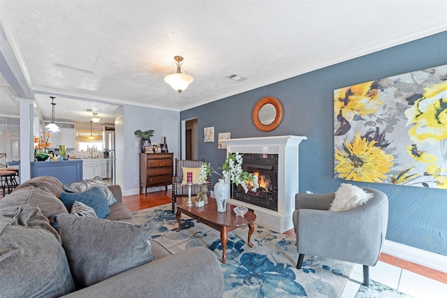 tiled living room featuring visible vents, crown molding, baseboards, decorative columns, and a warm lit fireplace