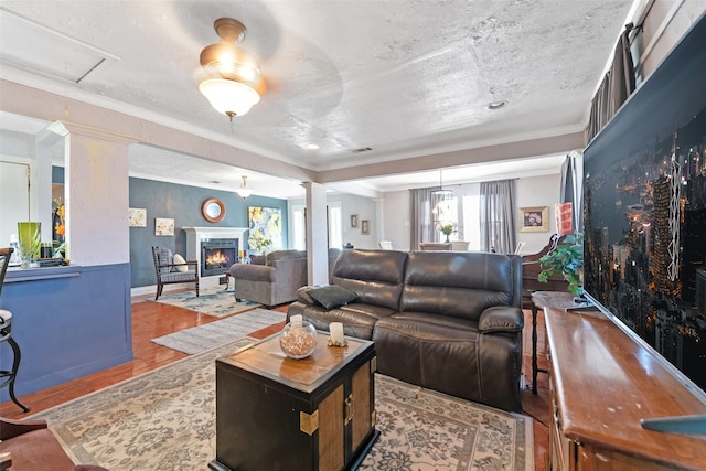 living room with visible vents, ornate columns, a lit fireplace, a textured ceiling, and crown molding