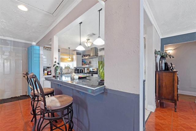 kitchen with a kitchen bar, stainless steel range oven, a textured ceiling, wall chimney exhaust hood, and crown molding