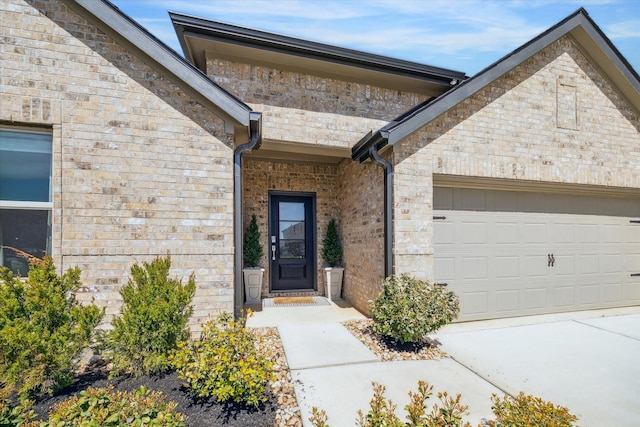 doorway to property featuring concrete driveway, an attached garage, and brick siding