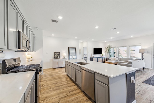 kitchen featuring visible vents, gray cabinets, a sink, stainless steel appliances, and open floor plan