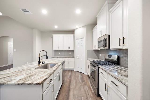 kitchen featuring visible vents, an island with sink, a sink, stainless steel appliances, and white cabinetry