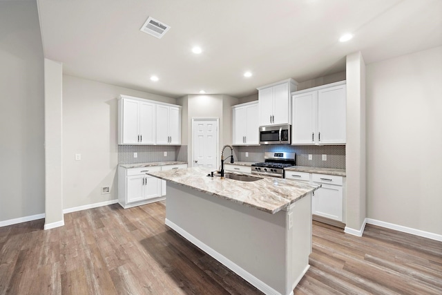 kitchen with visible vents, a kitchen island with sink, a sink, light wood-style floors, and appliances with stainless steel finishes