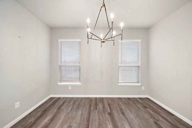 unfurnished dining area with dark wood finished floors, a notable chandelier, and baseboards