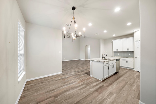 kitchen with arched walkways, a sink, white cabinets, stainless steel dishwasher, and light wood-type flooring