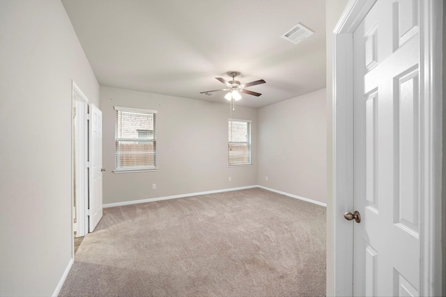 unfurnished room with visible vents, light colored carpet, baseboards, and a ceiling fan