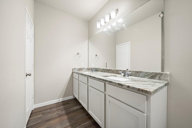 bathroom featuring double vanity, wood finished floors, baseboards, and a sink