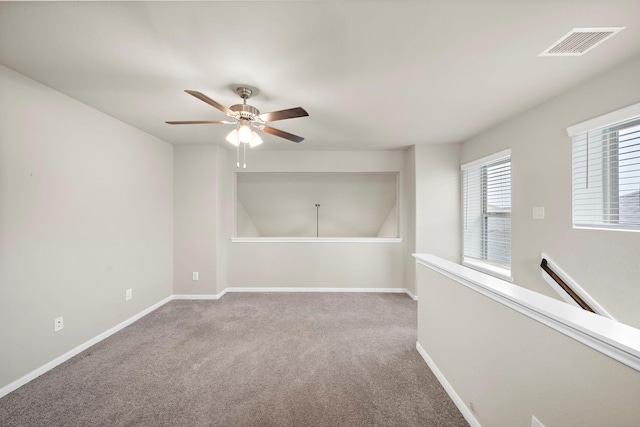 carpeted spare room featuring visible vents, baseboards, and ceiling fan