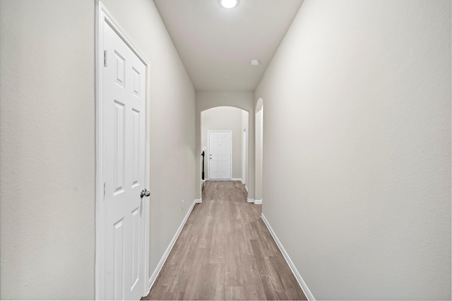 hall featuring baseboards, arched walkways, and wood finished floors