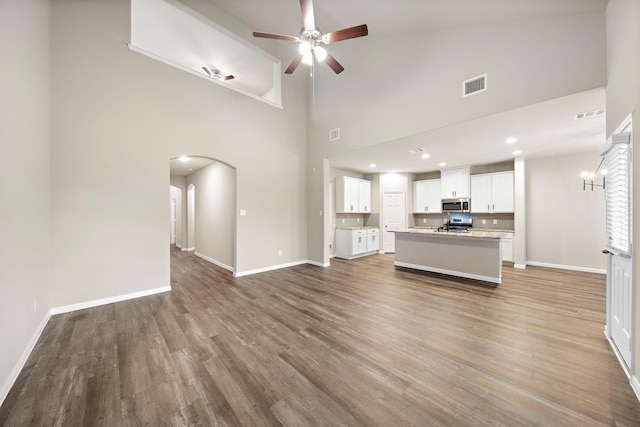 unfurnished living room featuring visible vents, baseboards, ceiling fan, light wood-style floors, and arched walkways