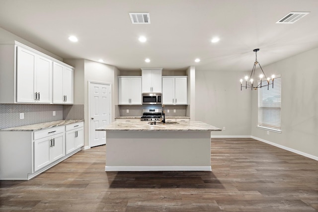 kitchen with stainless steel appliances, visible vents, wood finished floors, and decorative backsplash