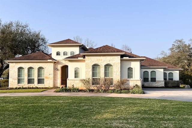 mediterranean / spanish-style home featuring stone siding, roof with shingles, and a front lawn