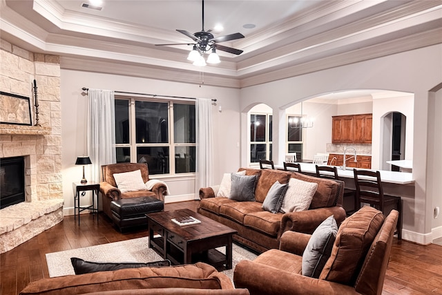 living room featuring a tray ceiling, arched walkways, dark wood-style floors, and ceiling fan