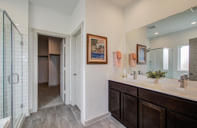 bathroom featuring a spacious closet, a shower stall, wood finished floors, and a sink