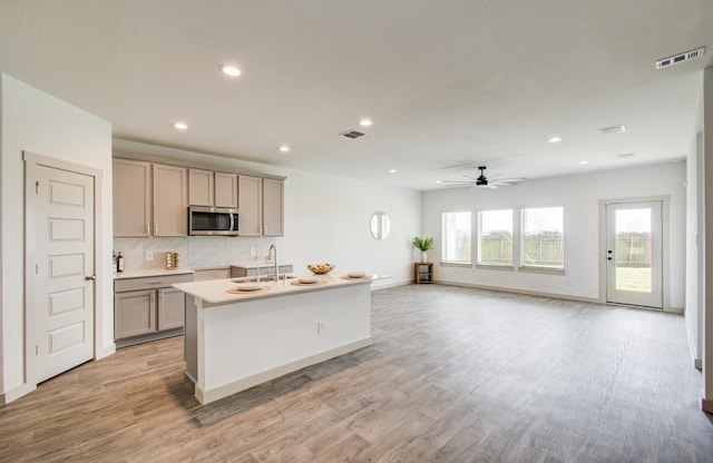 kitchen featuring stainless steel microwave, visible vents, gray cabinets, light wood-style flooring, and a ceiling fan