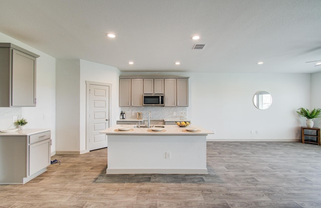 kitchen with visible vents, a sink, stainless steel microwave, backsplash, and light wood finished floors