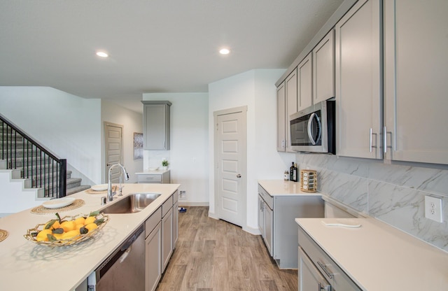 kitchen featuring gray cabinetry, a sink, light countertops, appliances with stainless steel finishes, and light wood-type flooring