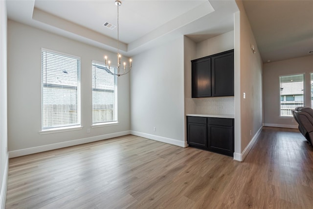 unfurnished dining area with a notable chandelier, baseboards, visible vents, and light wood finished floors