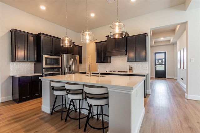 kitchen featuring a center island with sink, light countertops, light wood-style flooring, a kitchen breakfast bar, and stainless steel appliances