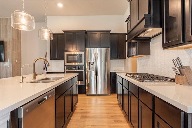 kitchen featuring a sink, range hood, light wood-style floors, appliances with stainless steel finishes, and light countertops