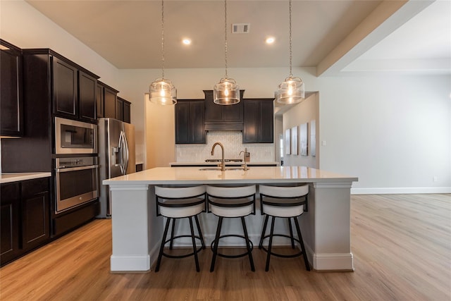 kitchen featuring visible vents, an island with sink, stainless steel appliances, light countertops, and backsplash