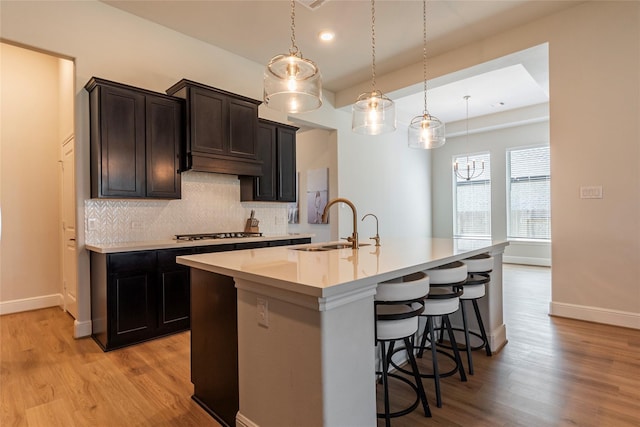 kitchen featuring decorative backsplash, light wood-style flooring, an island with sink, and a sink