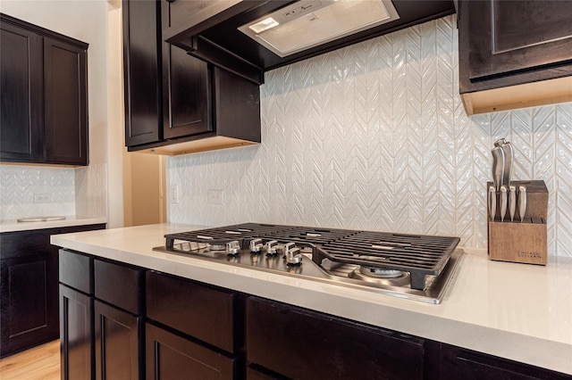 kitchen with backsplash, premium range hood, stainless steel gas cooktop, dark brown cabinetry, and light countertops