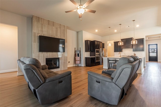 living area with light wood-style flooring, baseboards, ceiling fan, and a tile fireplace