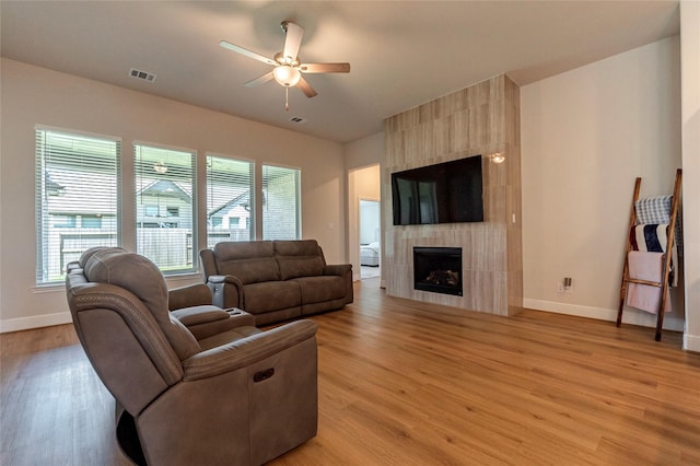 living room featuring visible vents, baseboards, ceiling fan, light wood-type flooring, and a fireplace