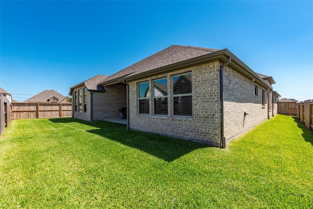 rear view of property with a yard, brick siding, a fenced backyard, and a shingled roof