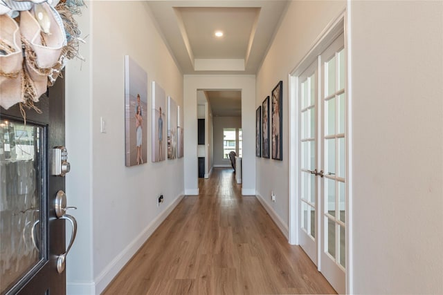 hallway featuring a raised ceiling, light wood-style floors, and baseboards