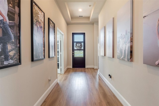 entryway with a tray ceiling, visible vents, baseboards, and wood finished floors